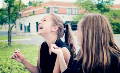Young girls inhaling vape in park.
